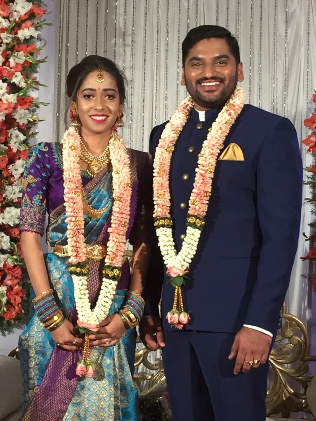 Garlanded bride and groom before a floral backdrop, Anubhandhaa Bangalore