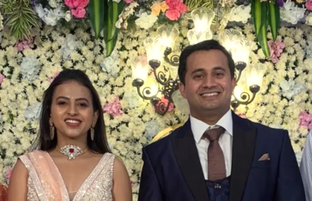 Smiling bride and groom before a floral wall at their reception, Anubhandhaa
